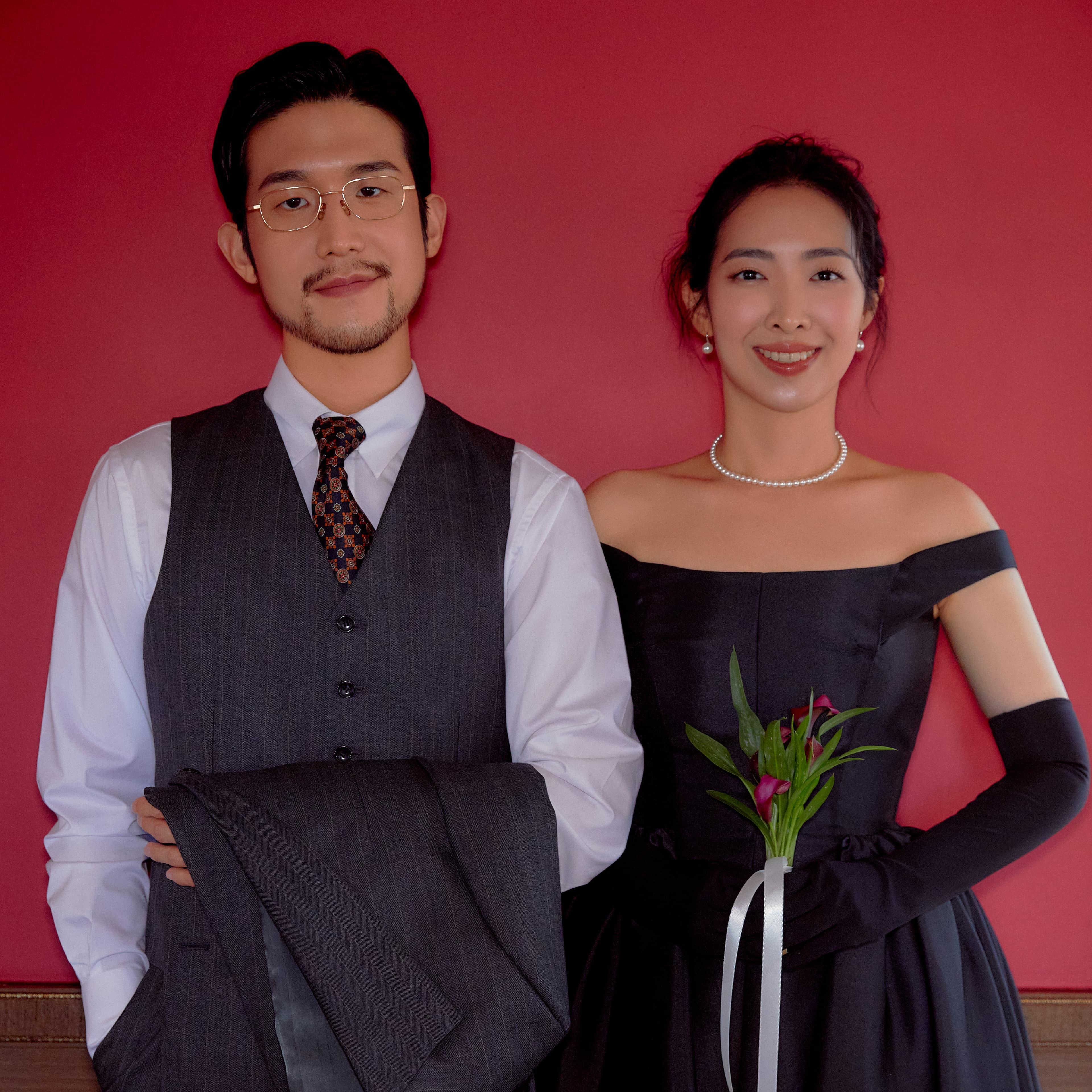 웨딩 사진 메인. 와인색 벽, 팔짱 끼고 있으며 신부는 부케를 들고 있다.