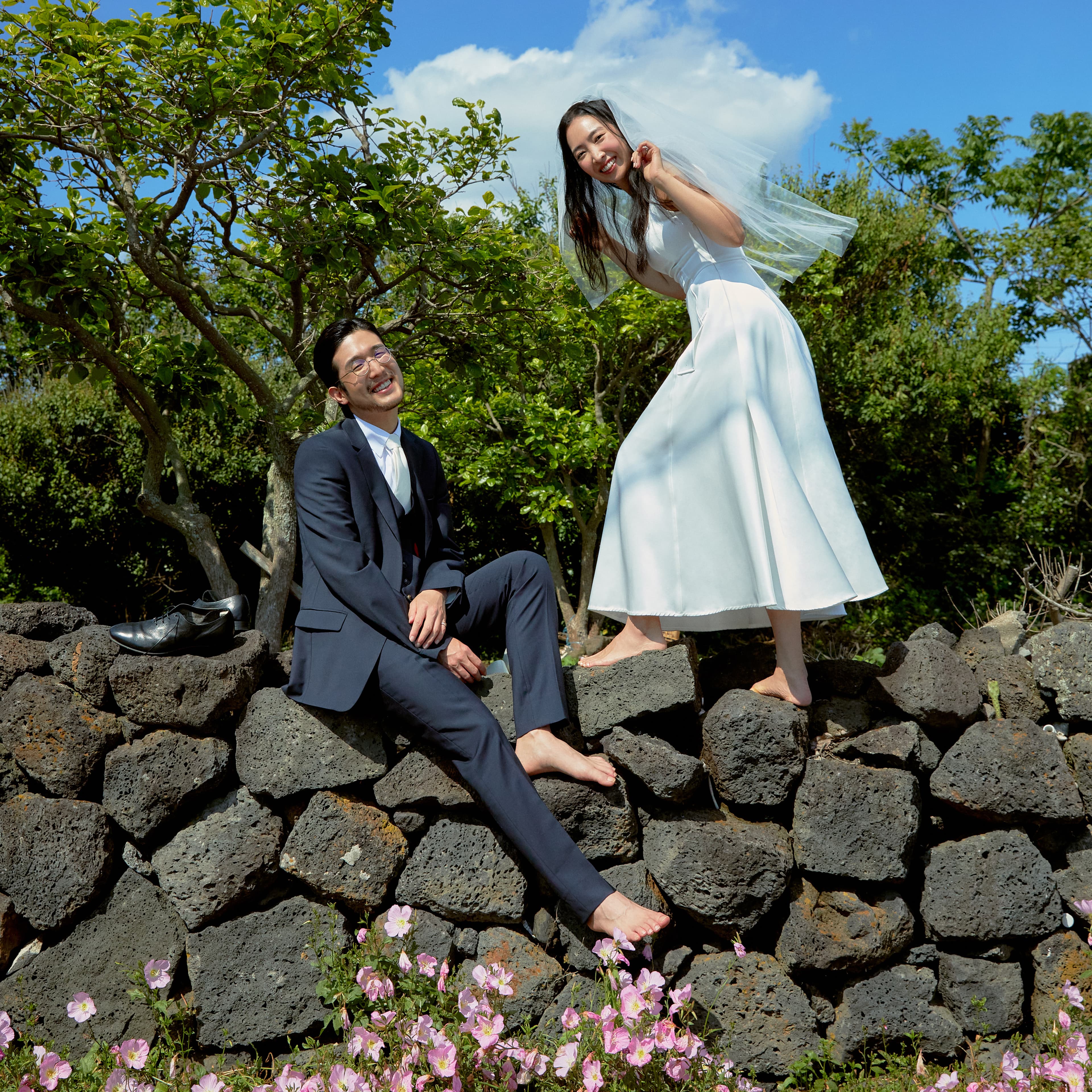 웨딩 사진 서브메인. 돌담에 현웅이 비스듬히 앉아있고, 도희가 같은 각도로 상체를 기울이며 서있다.