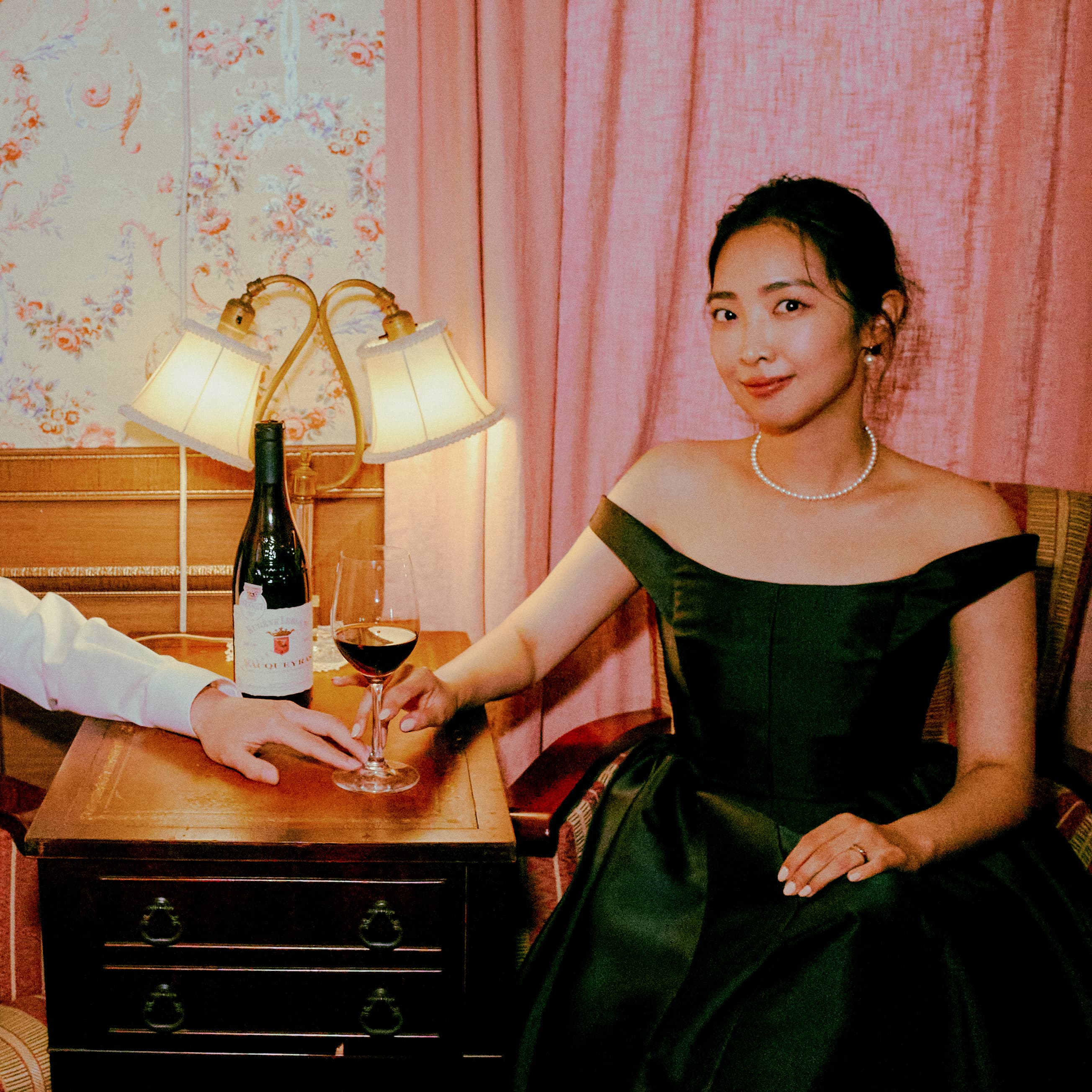 와인 테이블에 앉아 와인잔 위에서 손을 겹쳐 잡고 있다.